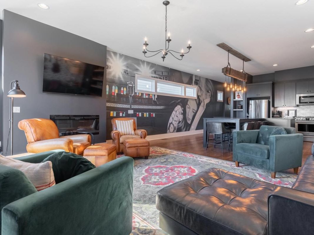 A spacious modern living area with leather and velvet seating, a bold wall mural, flat-screen TV, and an open-concept kitchen with stainless steel appliances.