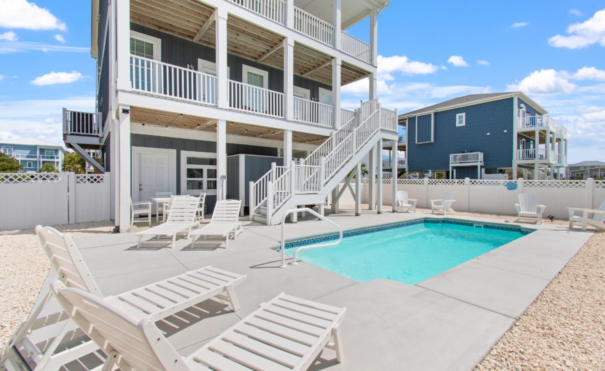 Modern beach rental with a private pool, surrounded by lounge chairs and white fencing for extra privacy. This dog-friendly retreat invites guests to unwind by the water and soak up the Carolina coast in comfort.