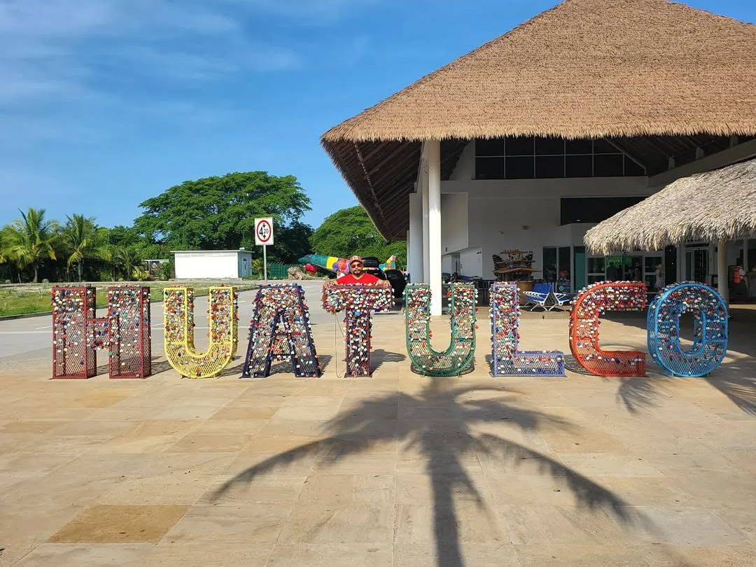 Colorful Huatulco letters outside the airport with palm trees and a bright blue sky, welcoming travelers upon arrival. A vibrant photo that captures the start of your Mexican beach getaway.