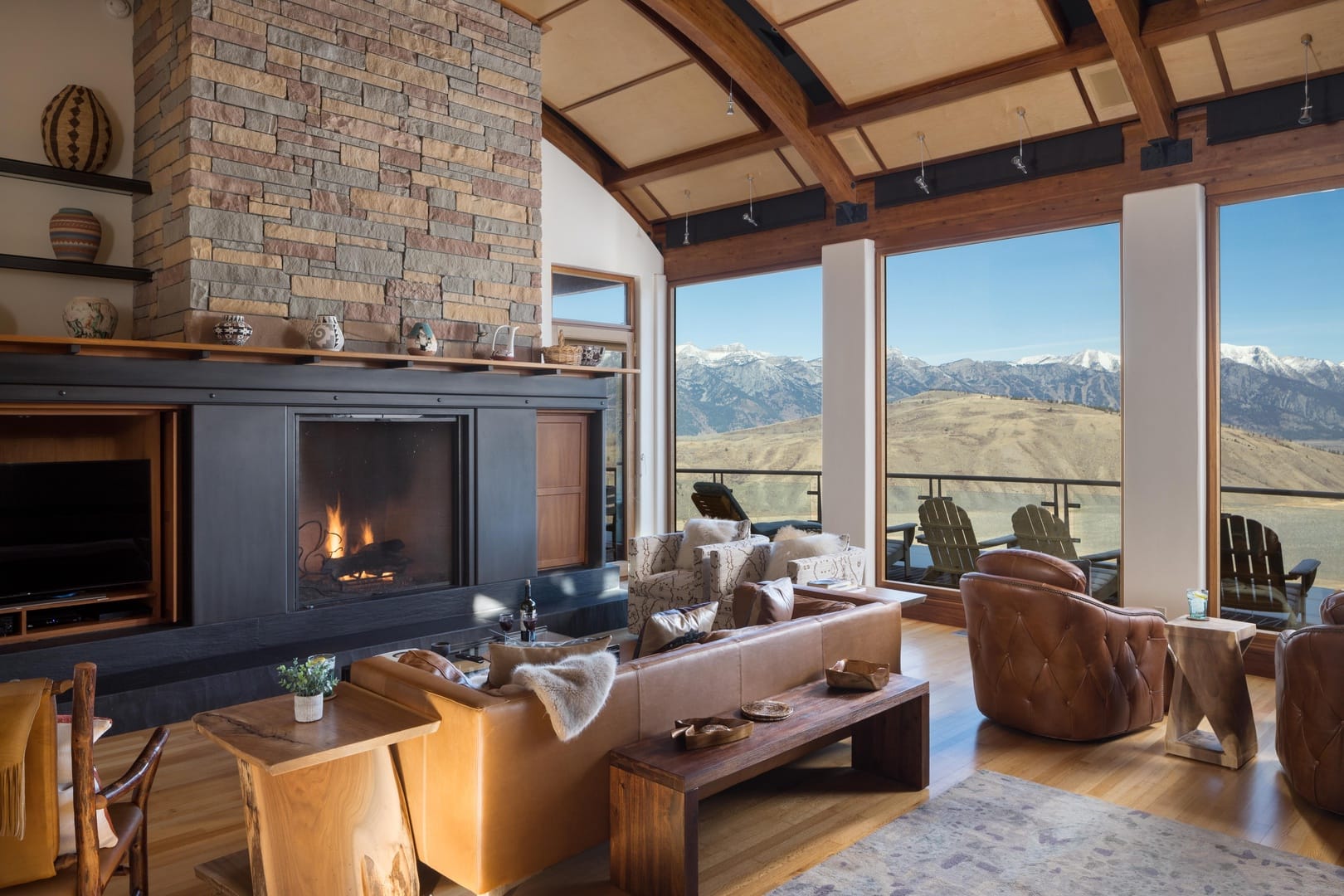 Interior of living room with black and stone-stacked fireplace, leather tan chairs, and open windows overlooking the mountains