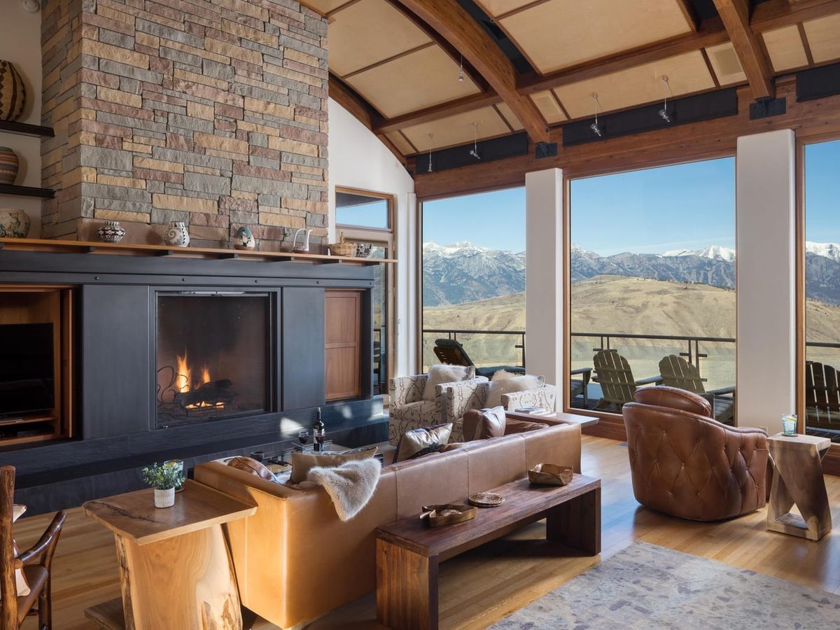 Interior of living room with black and stone-stacked fireplace, leather tan chairs, and open windows overlooking the mountains