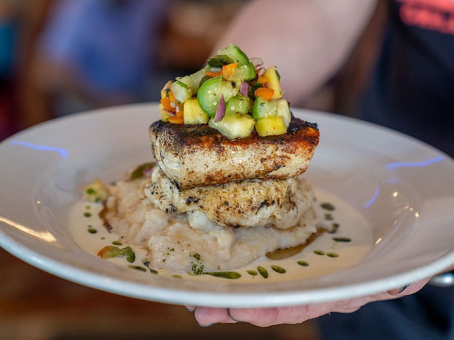 A perfectly seared salmon fillet is served over fresh asparagus and risotto at Kill Devil Grill. With sun-dried tomatoes and a lemon wedge on the side, this dish brings fine dining flavor to a laid-back beach spot.