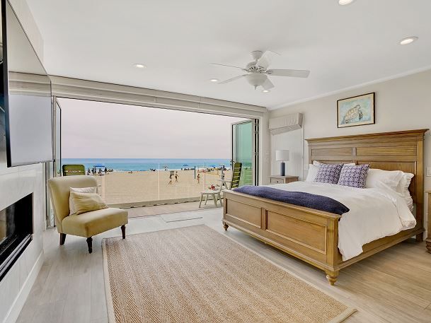 Oceanfront master bedroom in a Newport Beach vacation rental featuring a king bed, fireplace, and fully retractable glass doors opening directly to the beach.