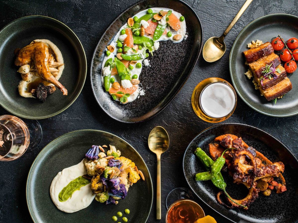 A vibrant table full of American and Mexican-inspired dishes including tacos, burgers, club sandwiches, and Cobb salad. Great for group lunches or family-style meals.