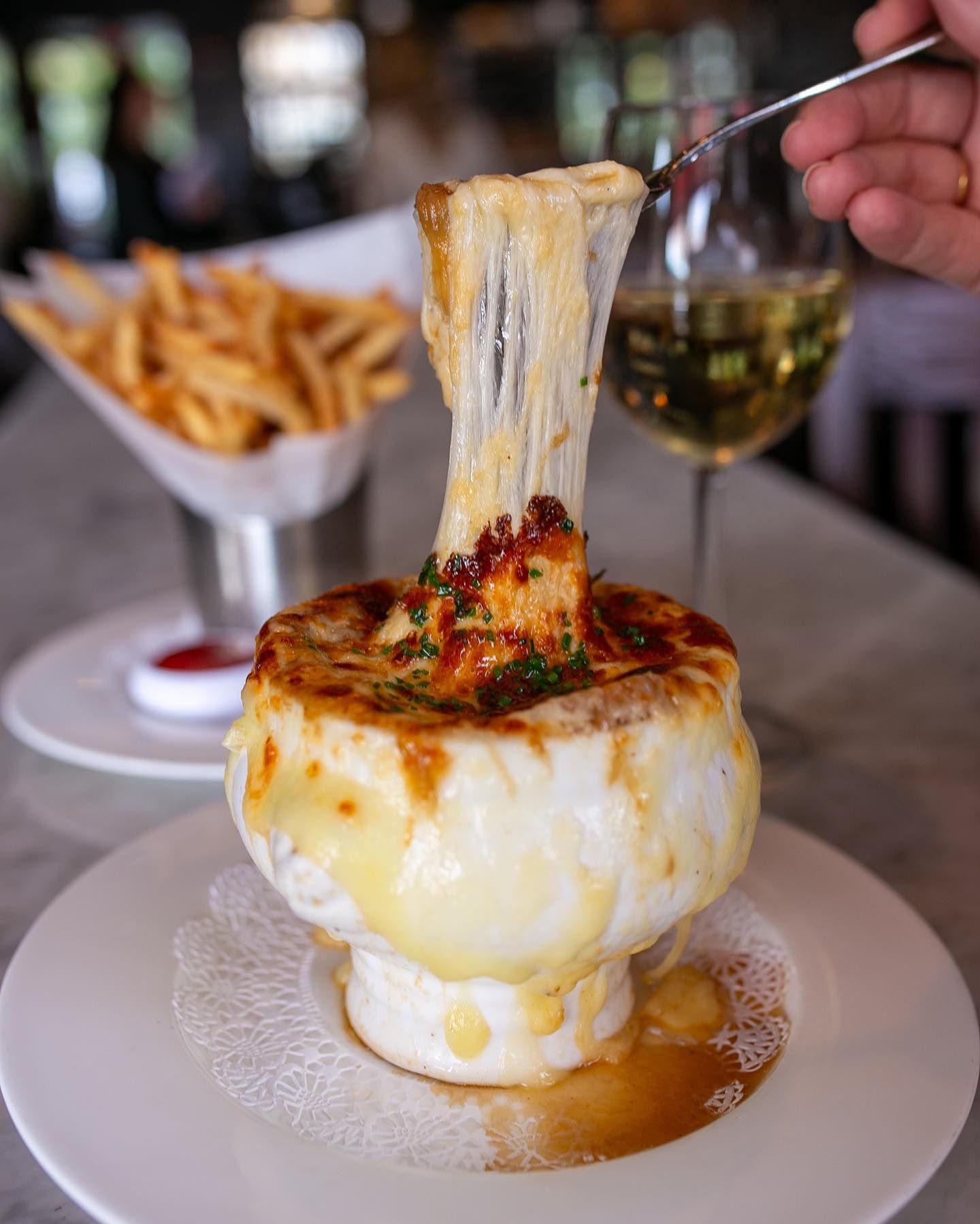 A bubbling bowl of French onion soup topped with golden melted cheese at Brasserie du Soleil. This cozy French bistro pairs rich flavors with elegant wines, perfect for a relaxed meal in Wilmington.