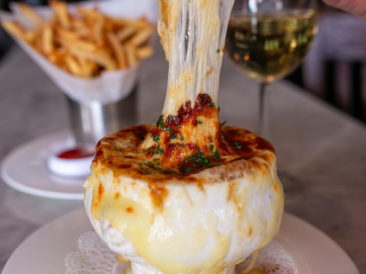 A bubbling bowl of French onion soup topped with golden melted cheese at Brasserie du Soleil. This cozy French bistro pairs rich flavors with elegant wines, perfect for a relaxed meal in Wilmington.