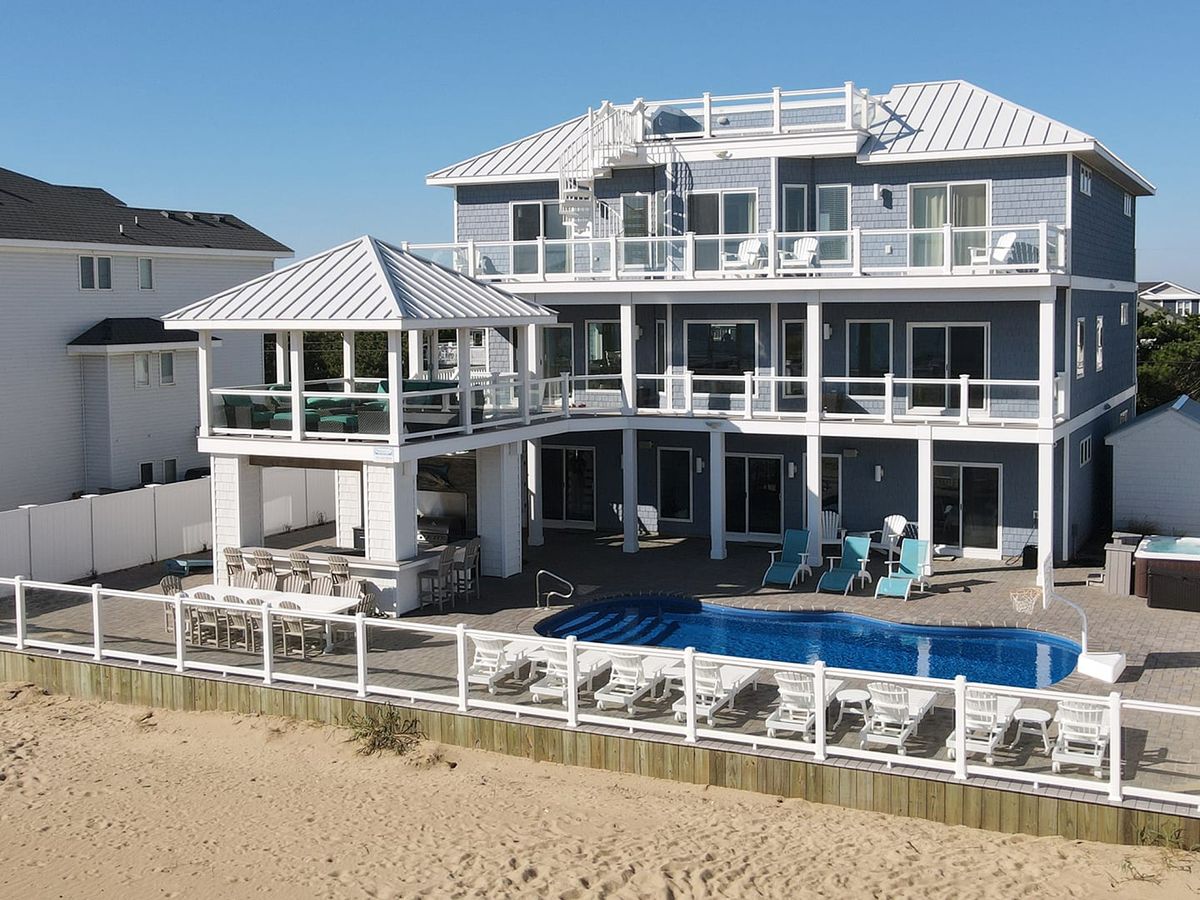 Luxury beach home with a spacious pool deck, sun loungers, and shaded seating. Perfect for large groups looking for a serene oceanfront escape.