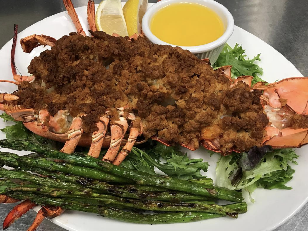 Stuffed baked lobster topped with golden breadcrumbs, served with grilled asparagus, lemon wedges, and a cup of melted butter on a bed of fresh greens.