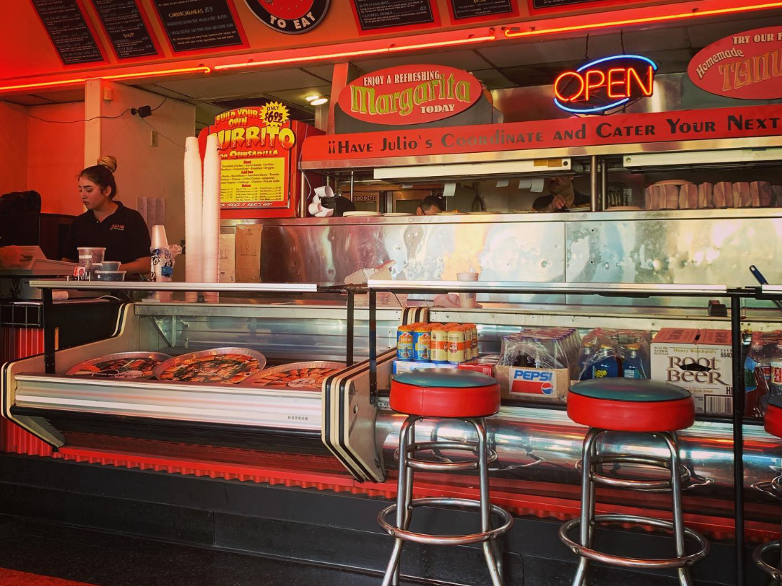 two old barstools next to counter at restaurant in arizona with neon open sign and red interior lighting