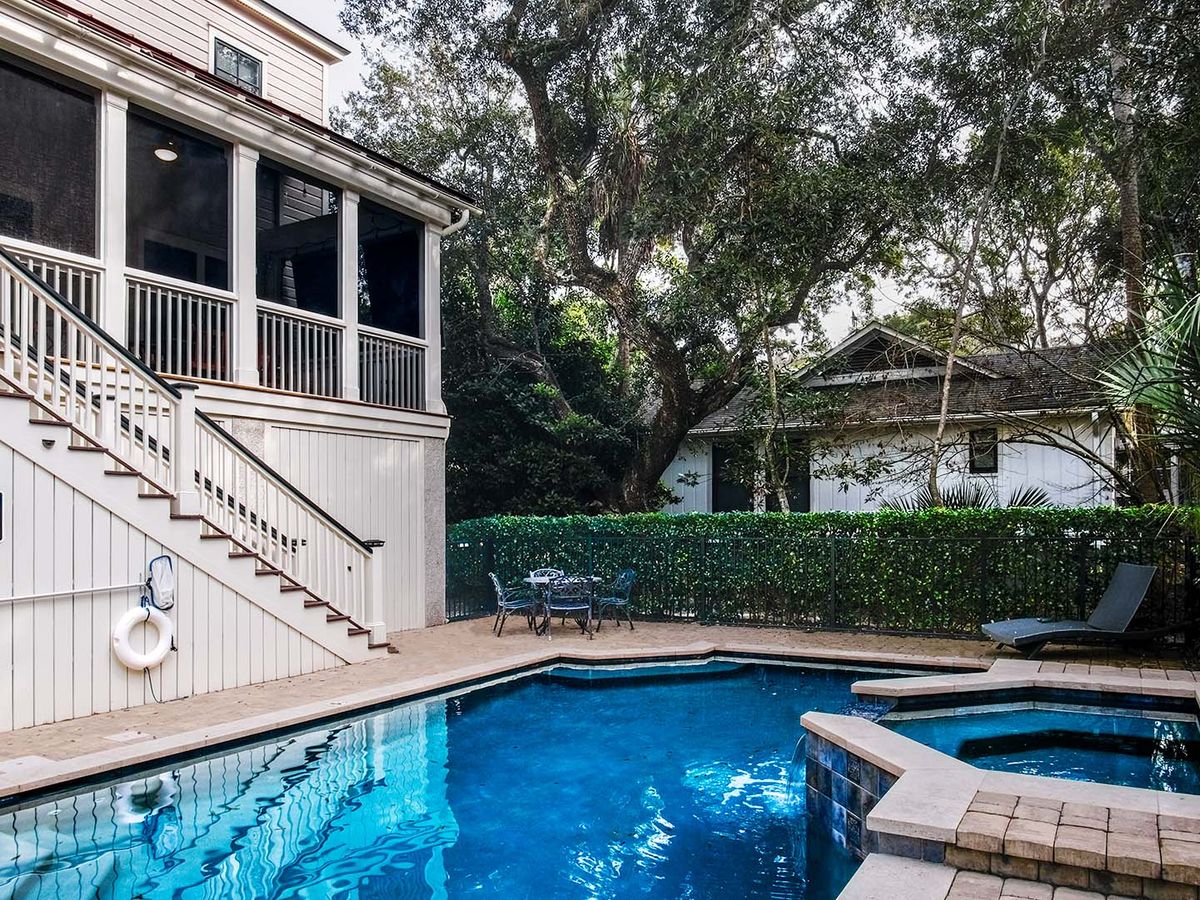 Private outdoor pool with attached hot tub, surrounded by a patio with seating, greenery, and a screened porch above.
