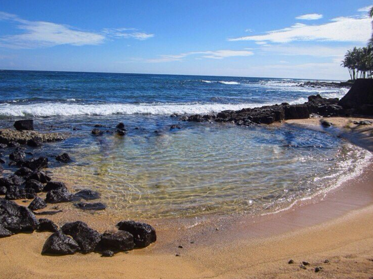 Ocean calmly on sandy shore with rocks surrounding it in hawai