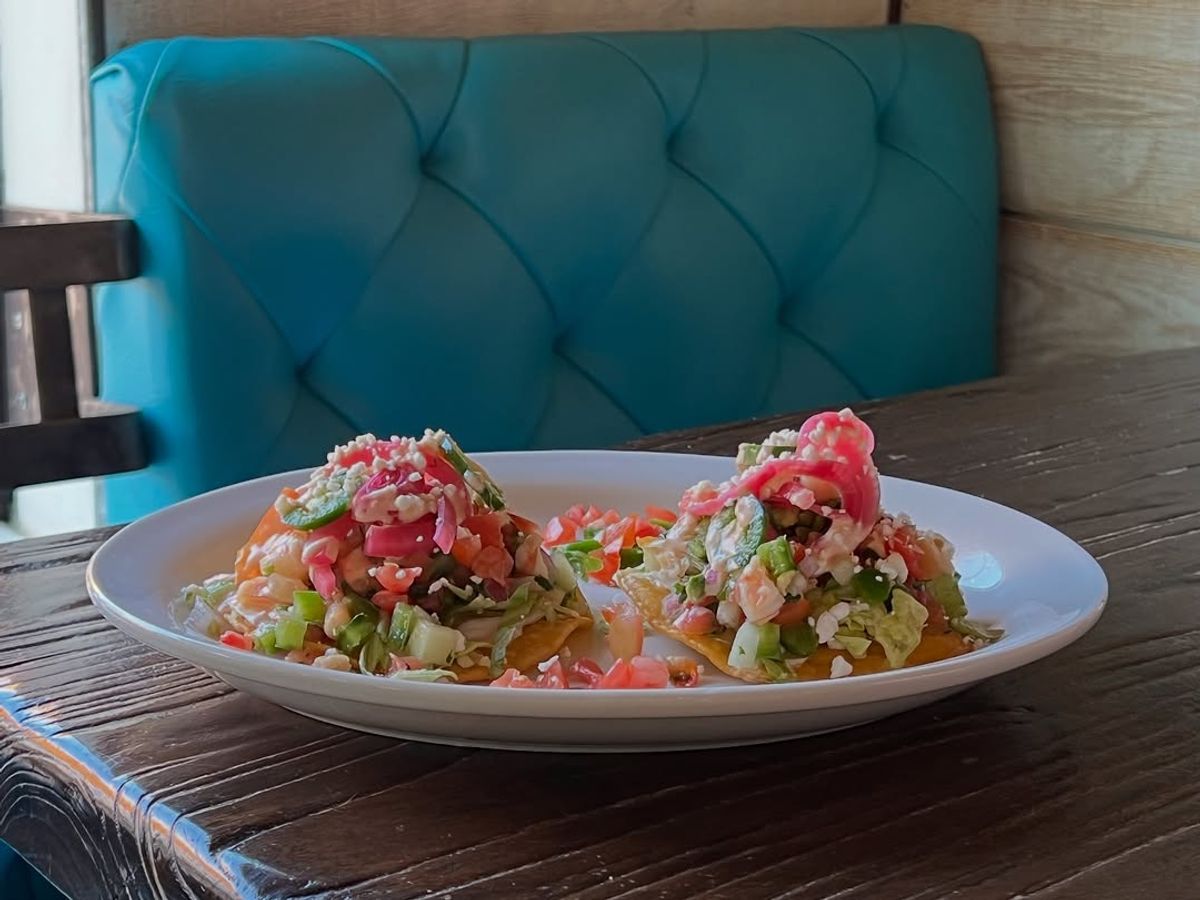 Two tostadas piled high with fresh ceviche, avocado, and pickled onions served in a cozy turquoise booth. A vibrant mix of flavor and color that celebrates coastal Mexican cuisine.