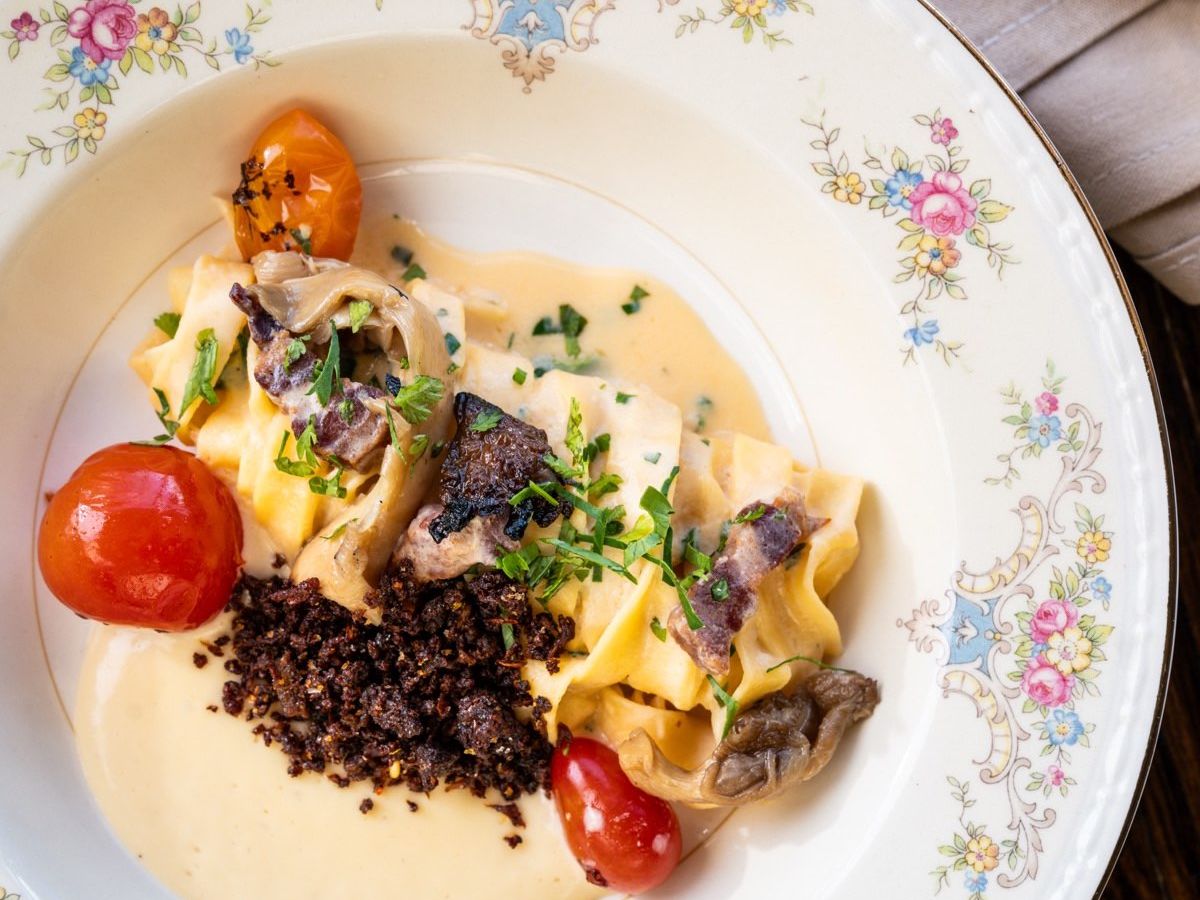 Fresh handmade pasta topped with mushrooms, herbs, and cherry tomatoes sits on a vintage floral plate. Patowmack Farm’s seasonal ingredients and artistic plating create an elegant farm-to-table experience.