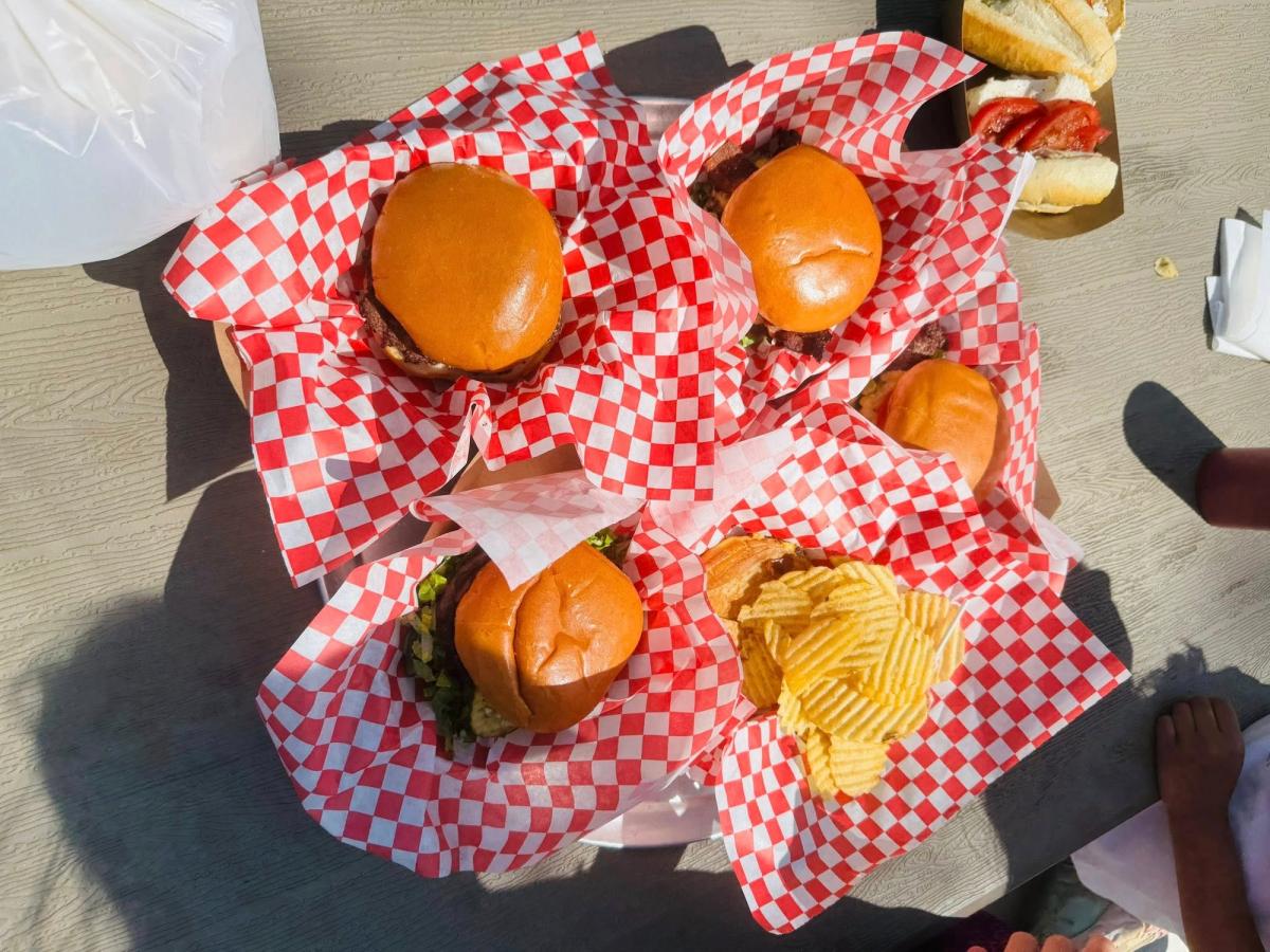 A tray of fresh-grilled burgers and rippled chips served in red-checkered baskets, ready for a casual picnic or family meal outdoors. A sunny day classic.