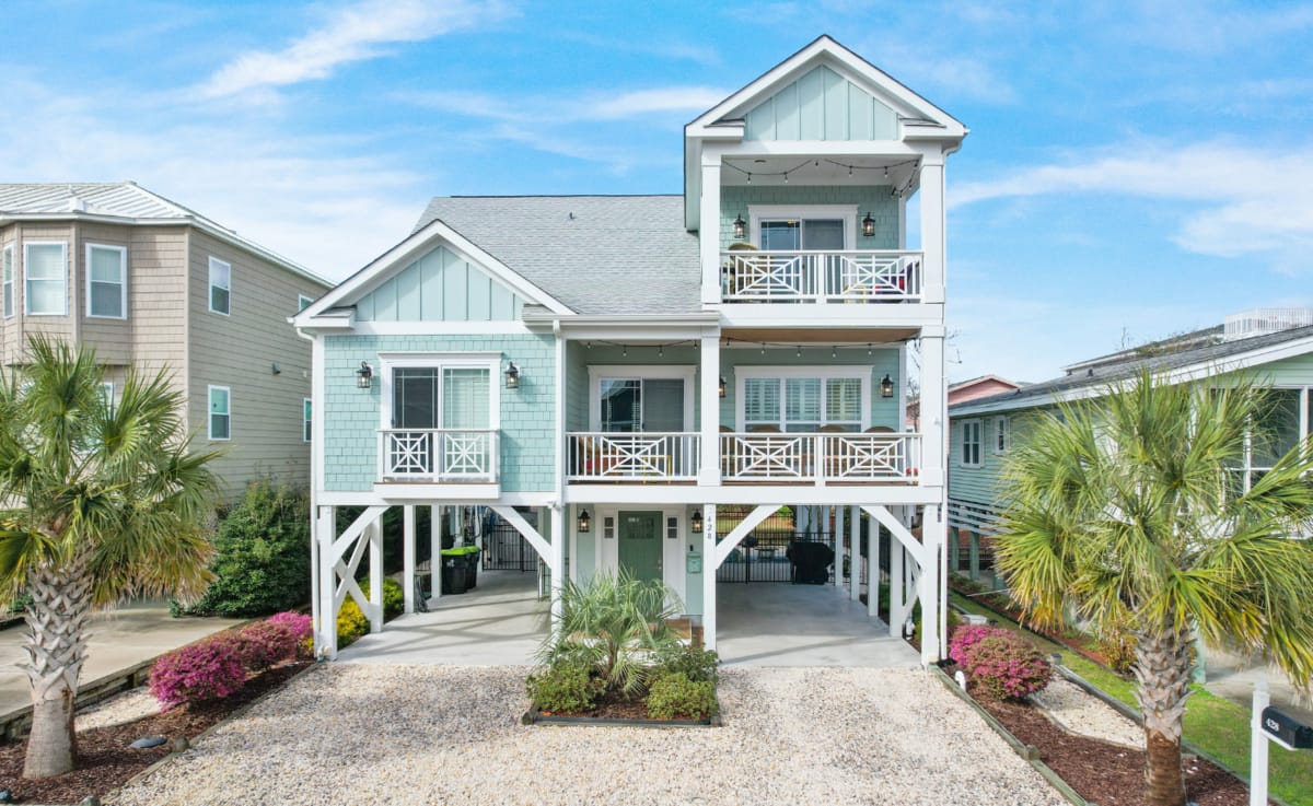 Beautiful stilted beach house framed by palm trees with classic coastal charm and bright turquoise siding. Its welcoming balconies and open design make it ideal for families wanting easy access to the sand and sunshine.