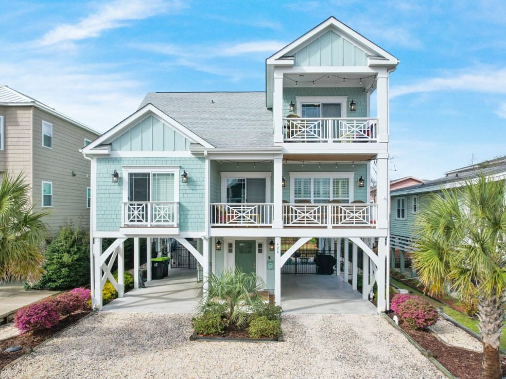 Beautiful stilted beach house framed by palm trees with classic coastal charm and bright turquoise siding. Its welcoming balconies and open design make it ideal for families wanting easy access to the sand and sunshine.