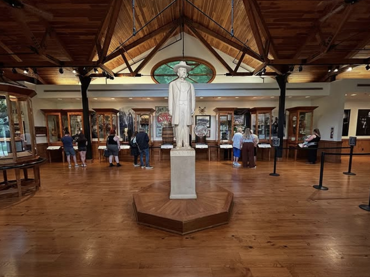 Visitors explore a museum exhibit with glass display cases and a central statue under a vaulted wooden ceiling.