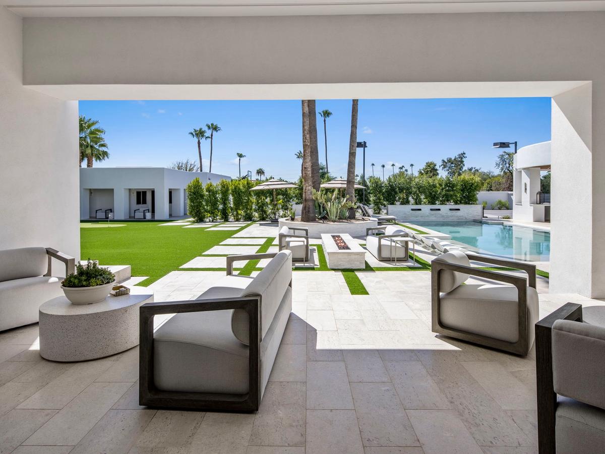 A modern luxury desert home patio with minimalist seating, a geometric lawn, fire feature, and pool framed by palm trees and clean white architecture.