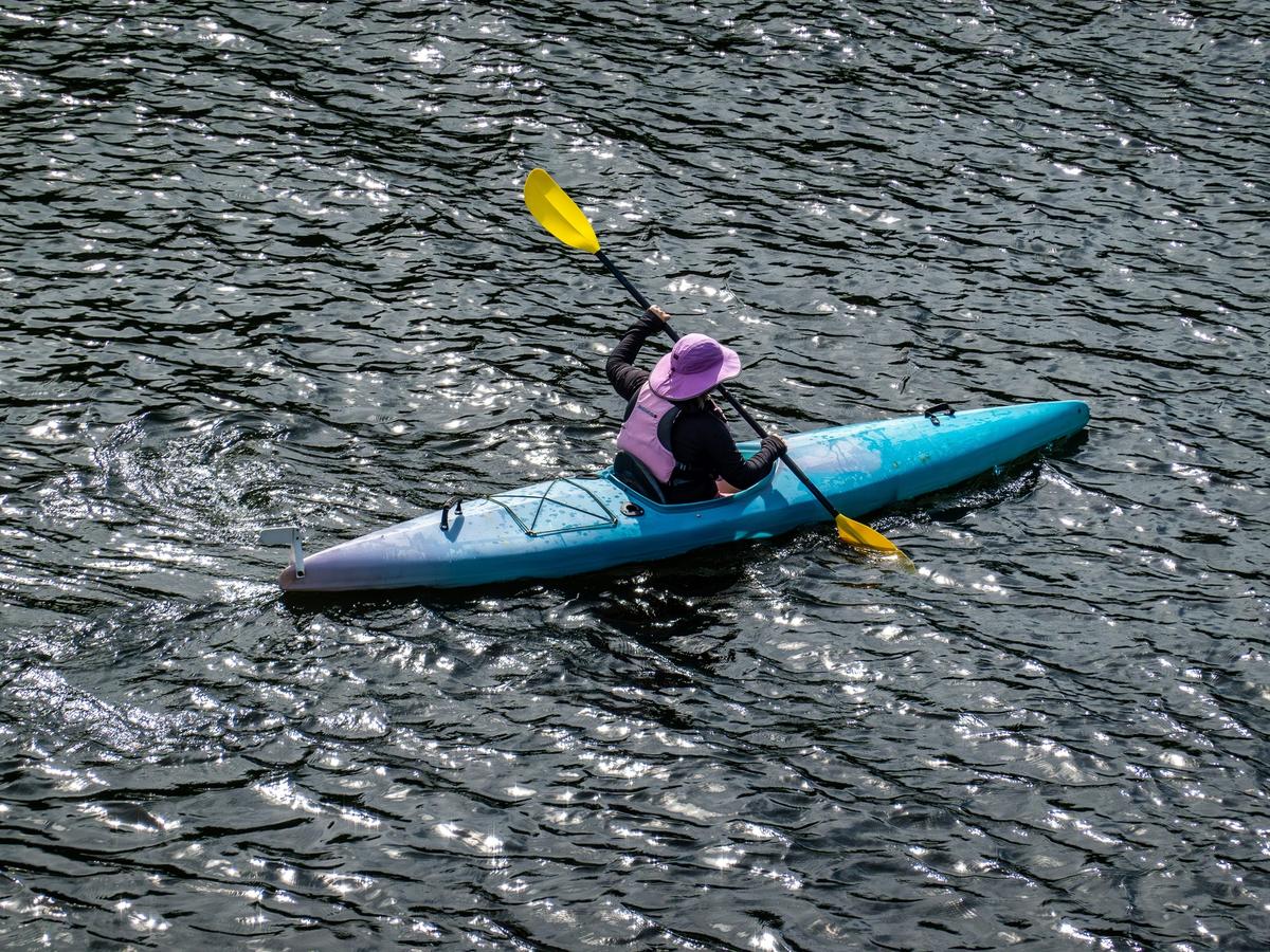Person wearing pink hat and long sleeve black shirt with kayak paddle in kayak on water