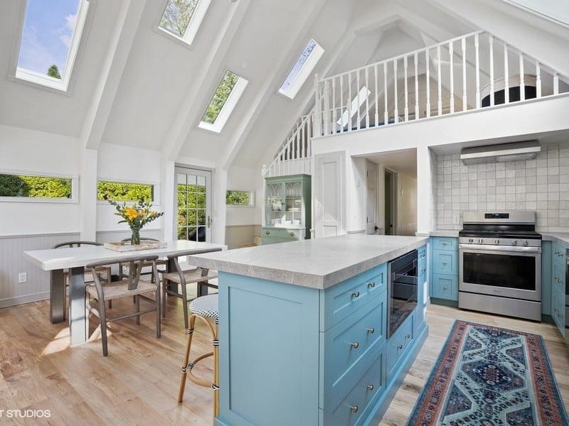 Bright and airy cottage kitchen with sky-high ceilings, blue cabinets, and natural light pouring in from skylights, ideal for morning pancakes and pup cuddles by the table. Just a block from the beach, it’s a peaceful retreat for both pets and people.