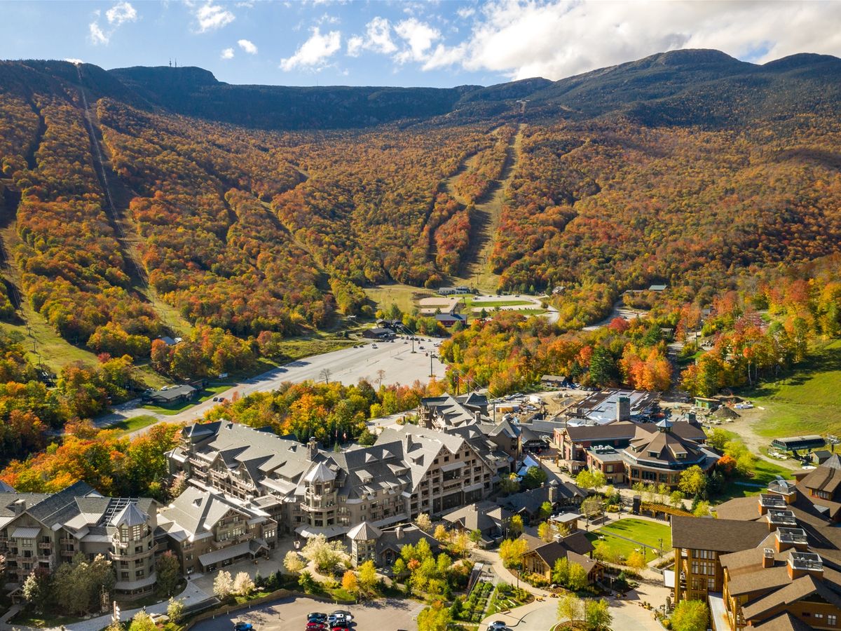 Aerial view of a picturesque mountain resort nestled at the base of tree-covered slopes bursting with fall foliage.