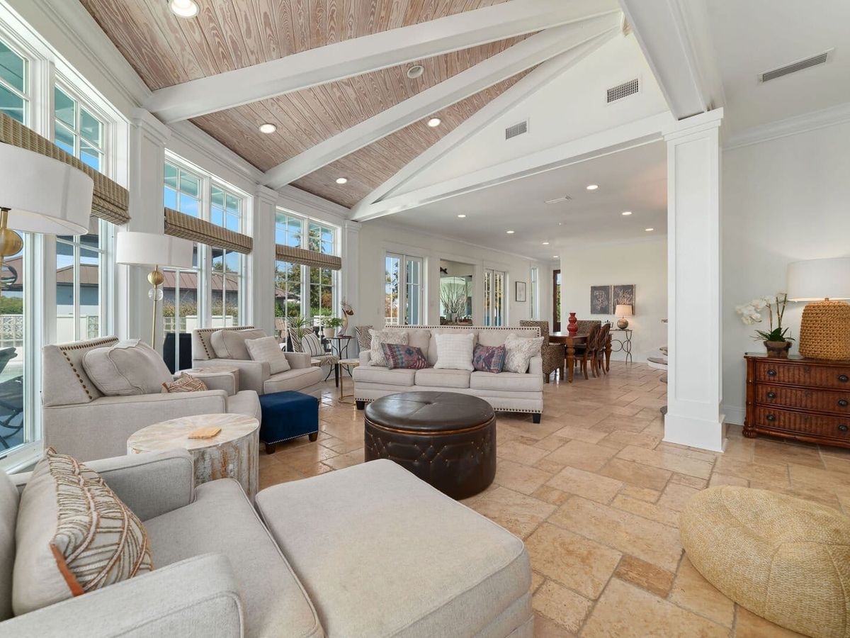 Elegant living space with vaulted wood ceilings, large windows, and neutral-toned seating. The open layout flows into a dining area, creating a bright and inviting setting.