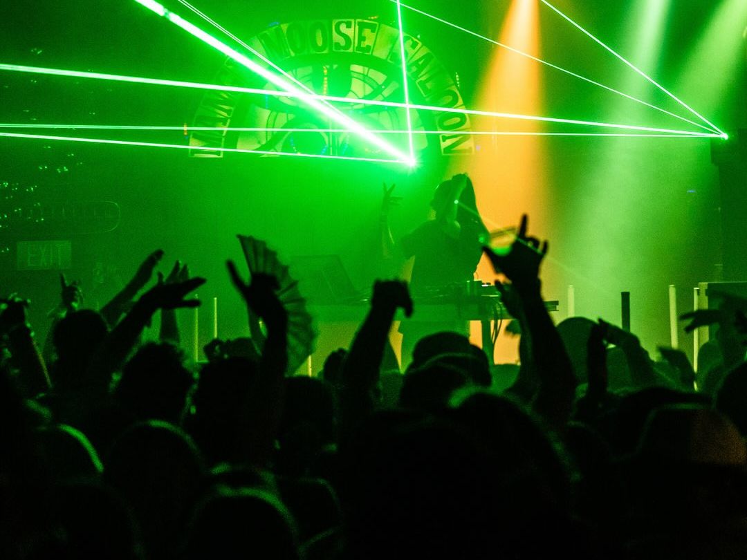 A DJ performs on stage at The Mangy Moose while the crowd raises their hands under purple concert lights. This popular après-ski spot in Teton Village is famous for live music, DJs, and unforgettable nights after the slopes close.