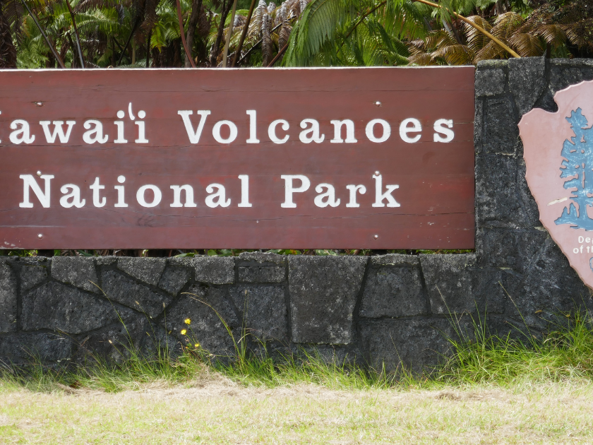 A rustic wooden sign marks the entrance to Hawaiʻi Volcanoes National Park, surrounded by lush greenery and tropical plants. A must-visit destination for seeing real lava fields and craters up close.