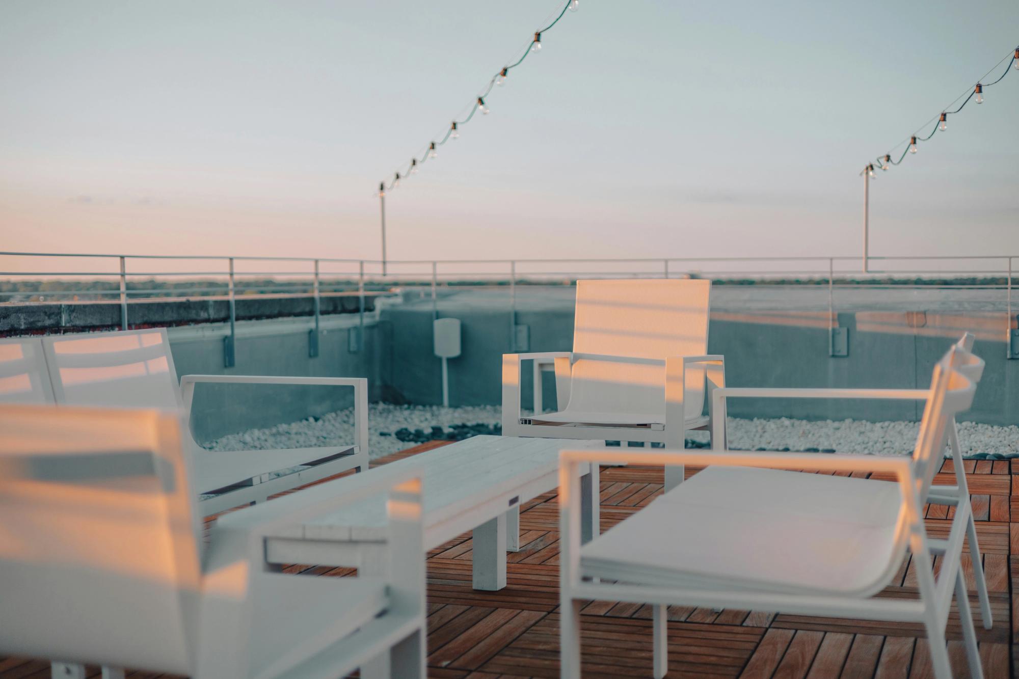 Rooftop patio at sunset with modern white chairs, a wooden deck, and string lights overhead.