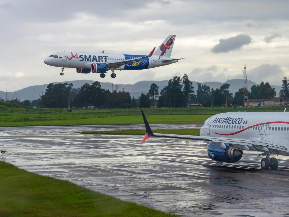 A JetSMART airplane landing while an AeroMexico plane waits on the runway, showing flights arriving into Huatulco. The cloudy skies and green landscape set the scene for arrival in Mexico.