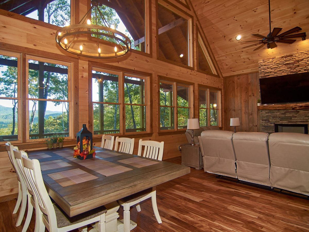Open-concept cabin with a wall of windows and forest views, plus comfy leather seating near a stone fireplace. Whether you’re soaking in the hot tub or playing pool, this cabin blends fun and peace.