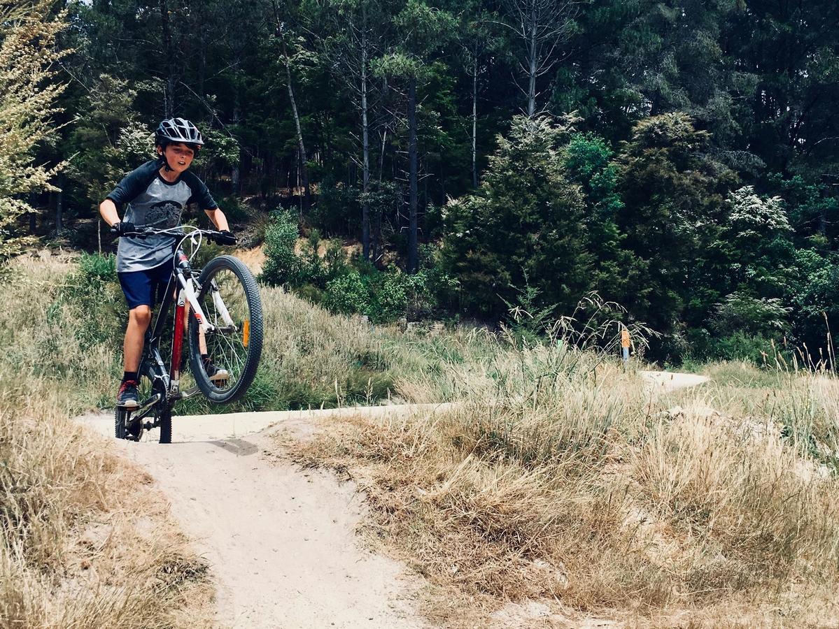 Bike trail adventure with a young rider pulling a wheelie along a dirt path in the middle of nature.
