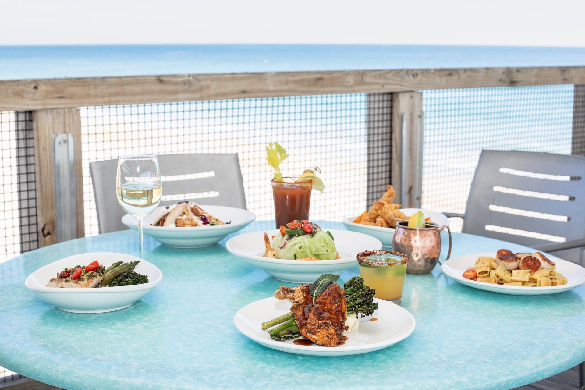 Plates of fresh seafood and salads set on a turquoise table overlooking the ocean at Oceanic Restaurant. With views of Crystal Pier and a beach breeze, it’s the perfect spot for coastal dining with a drink in hand.