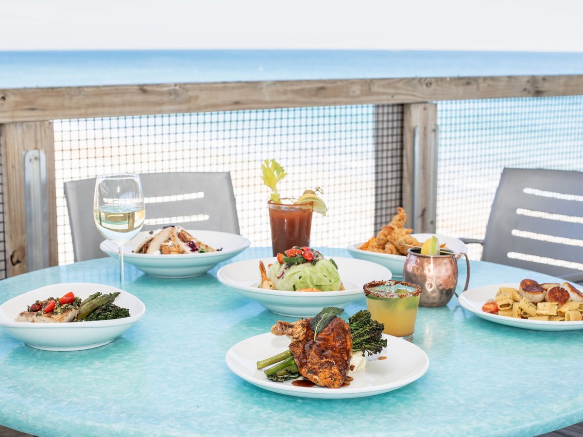 Plates of fresh seafood and salads set on a turquoise table overlooking the ocean at Oceanic Restaurant. With views of Crystal Pier and a beach breeze, it’s the perfect spot for coastal dining with a drink in hand.
