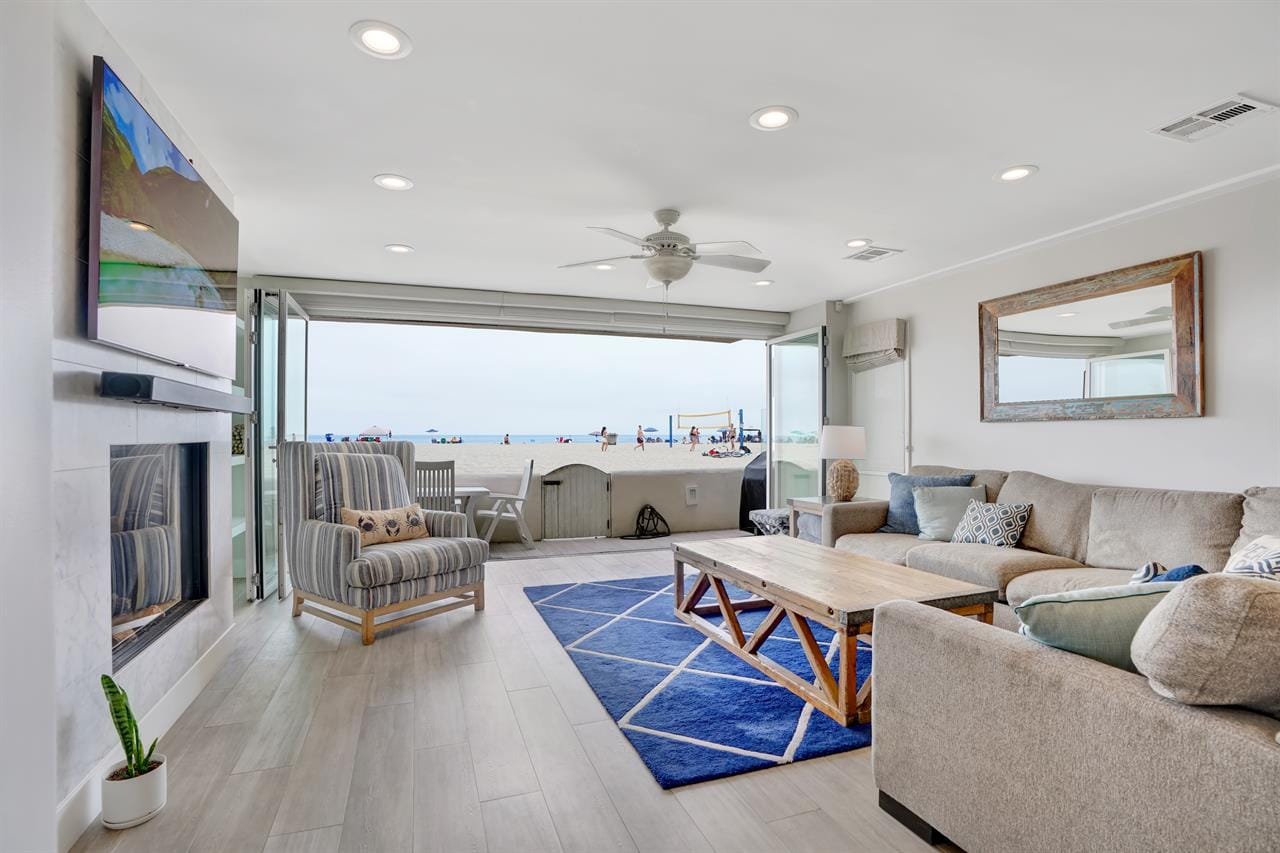 A bright beach house living room opens right onto the sand, with big folding doors bringing in the ocean breeze. Soft neutral furniture and beach views make the room feel fresh and relaxing. It’s perfect for watching the action right outside on the beach.