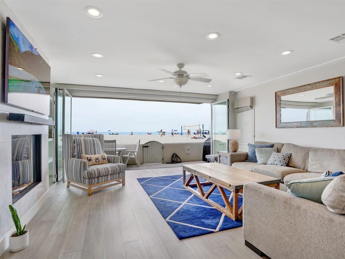 A bright beach house living room opens right onto the sand, with big folding doors bringing in the ocean breeze. Soft neutral furniture and beach views make the room feel fresh and relaxing. It’s perfect for watching the action right outside on the beach.