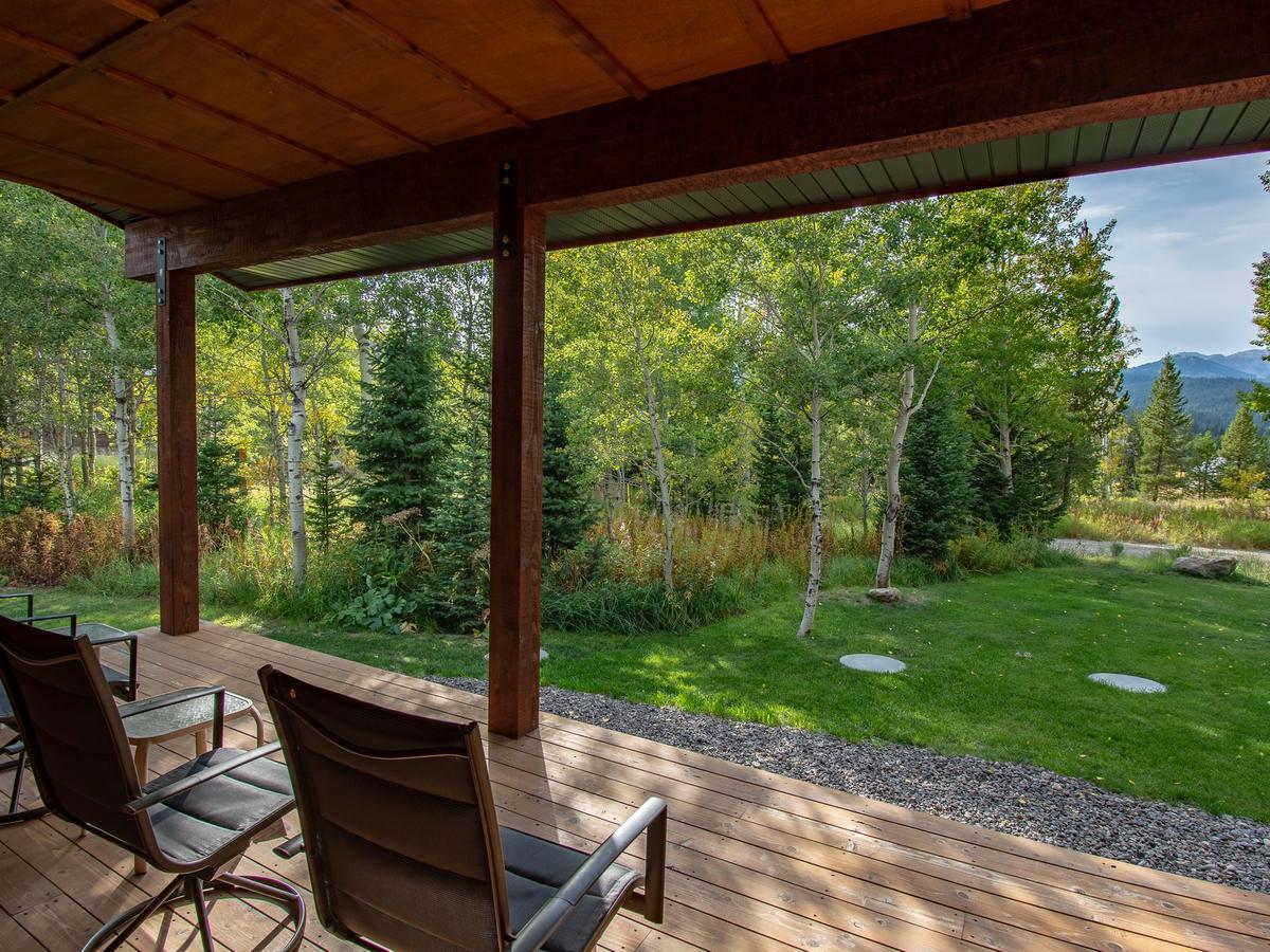 Covered wooden porch with several black chairs overlooking a grassy yard and forested landscape with distant mountain views.