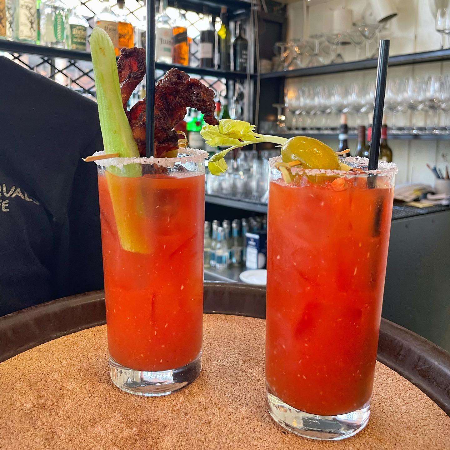Two bold Bloody Mary cocktails topped with celery and bacon sit at the bar at Cafe Pasqual’s in Santa Fe. The vibrant drinks reflect the city’s colorful Southwestern style. It’s a popular brunch and cocktail spot in downtown Santa Fe.