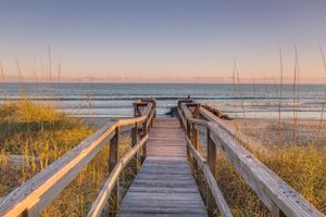 Wooden boardwalk leading to the ocean with waves crashing into the shore and sand on the beach