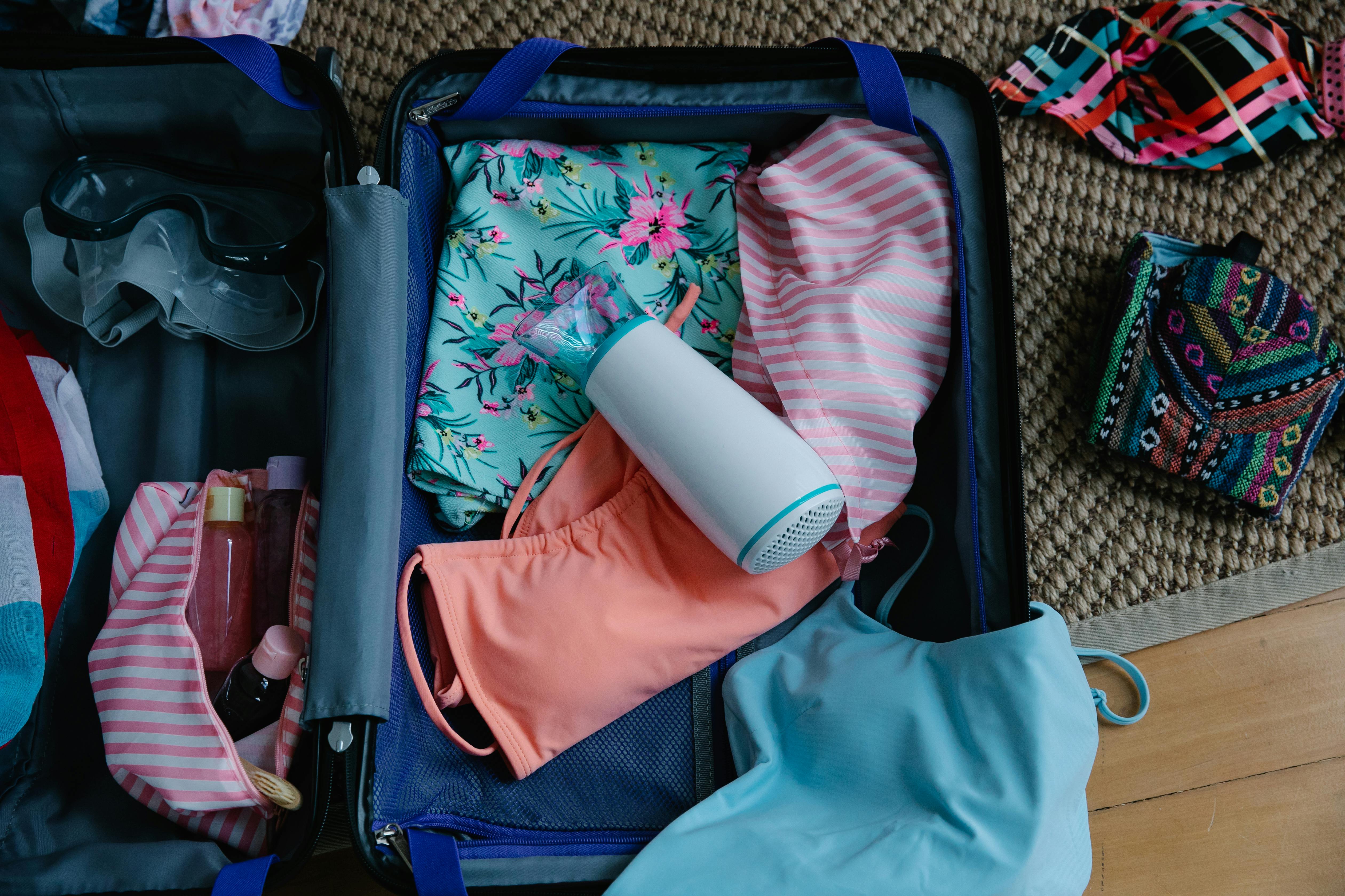 A neatly packed suitcase filled with colorful swimsuits, a floral cover-up, and travel essentials, ready for a beach getaway. The mix of vibrant patterns and soft fabrics captures the excitement of preparing for a coastal escape.