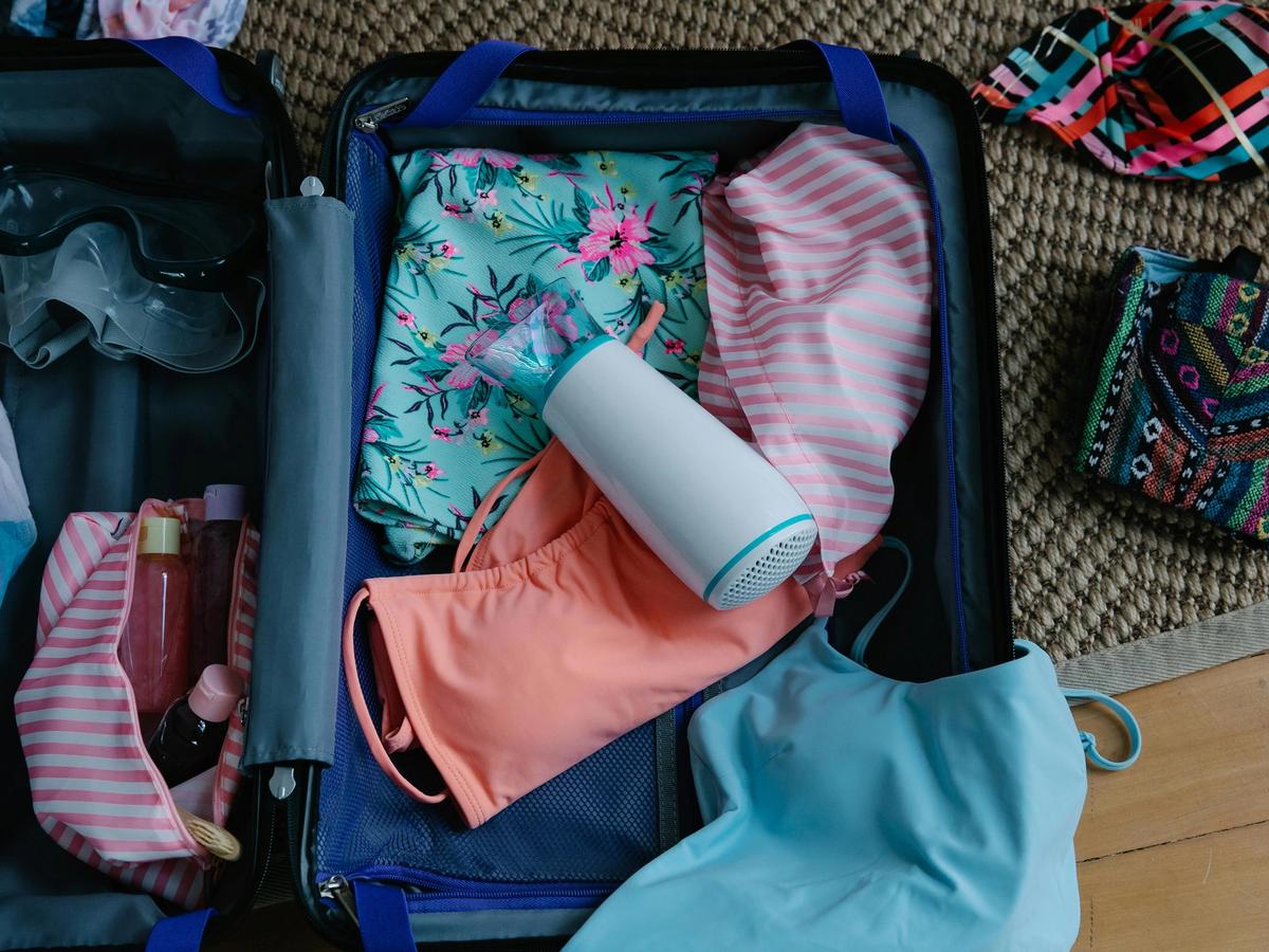 A neatly packed suitcase filled with colorful swimsuits, a floral cover-up, and travel essentials, ready for a beach getaway. The mix of vibrant patterns and soft fabrics captures the excitement of preparing for a coastal escape.