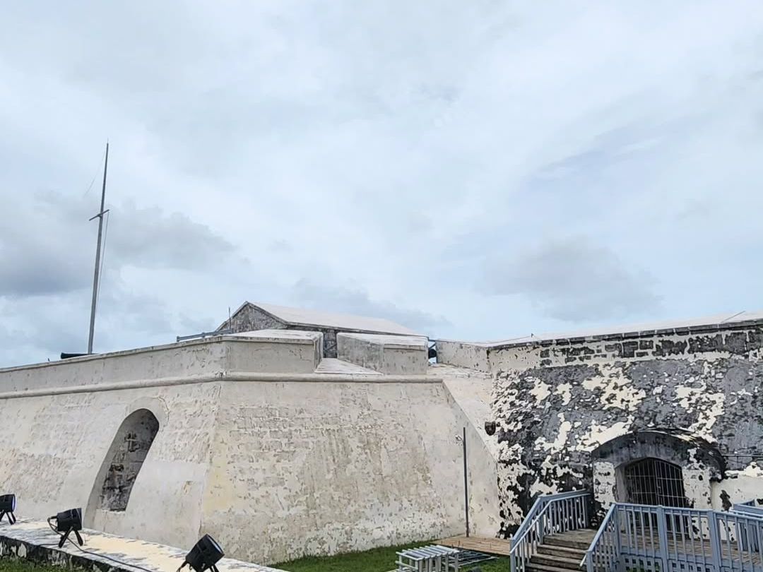 ort Charlotte, Nassau Bahamas' old stone fort with thick whitewashed walls stands under a cloudy sky, showing signs of age and history. The curved structure, arched entry, and raised walkway highlight its military design and coastal defense past. This historic fort feels quiet, weathered, and full of local heritage.