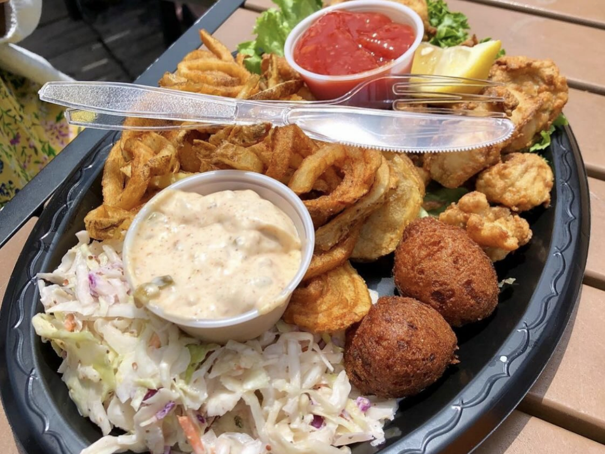 A seafood platter featuring fried shrimp and oysters, hush puppies, seasoned curly fries, coleslaw, and dipping sauces served on a black plate.