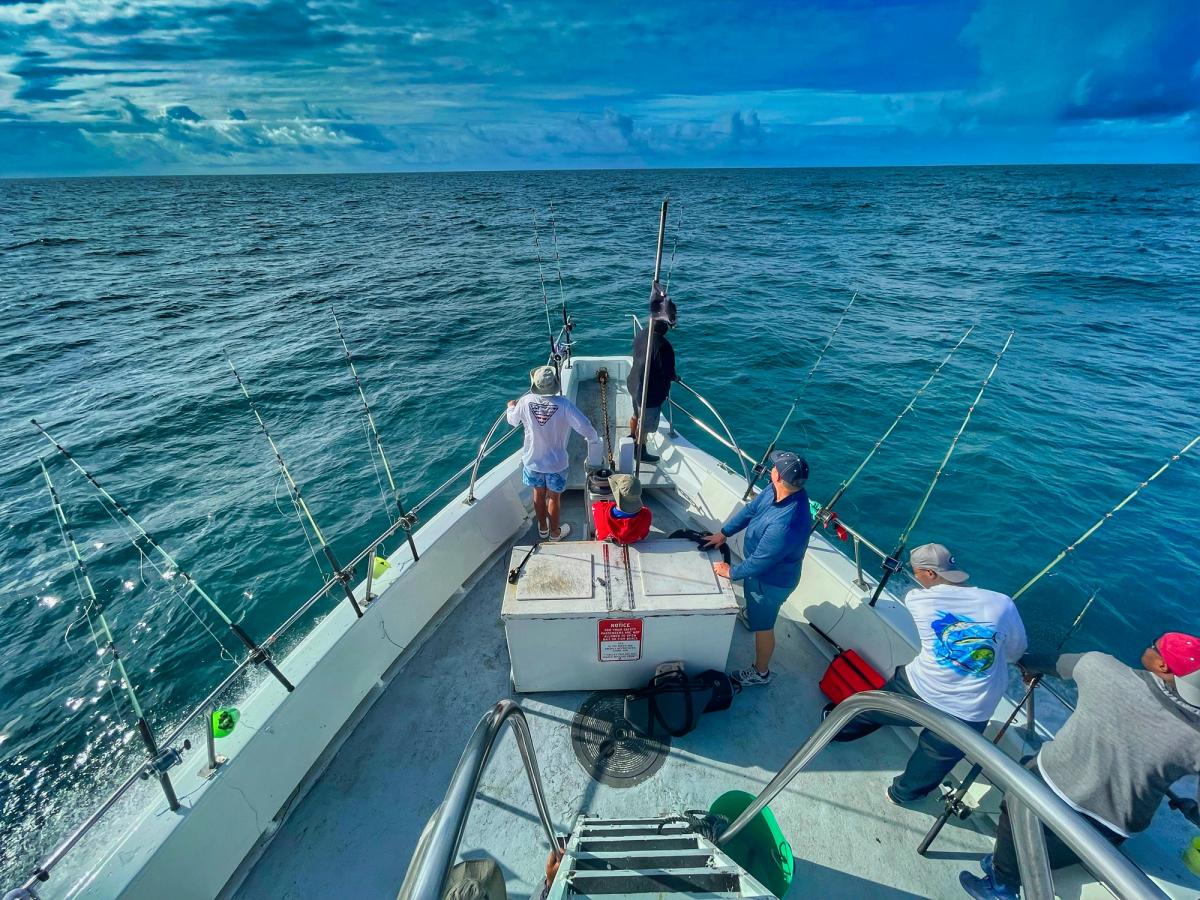 Group of men in fishing shirts on deep-sea fishing boat with rods on the sides of the boat and cloudy skies