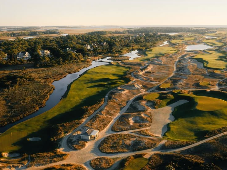Aerial view of golf course with beach on one side and river on the other