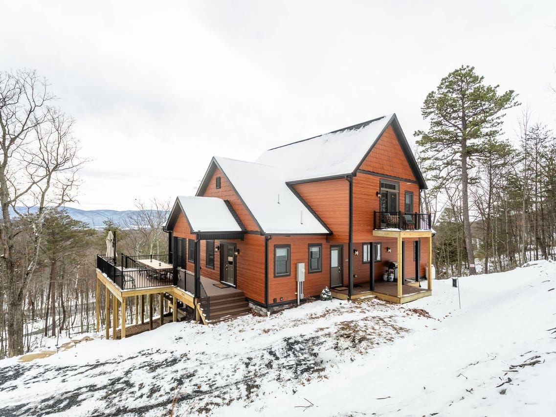 View of snowy cabin rental with snow surrounding the area and trees around the home