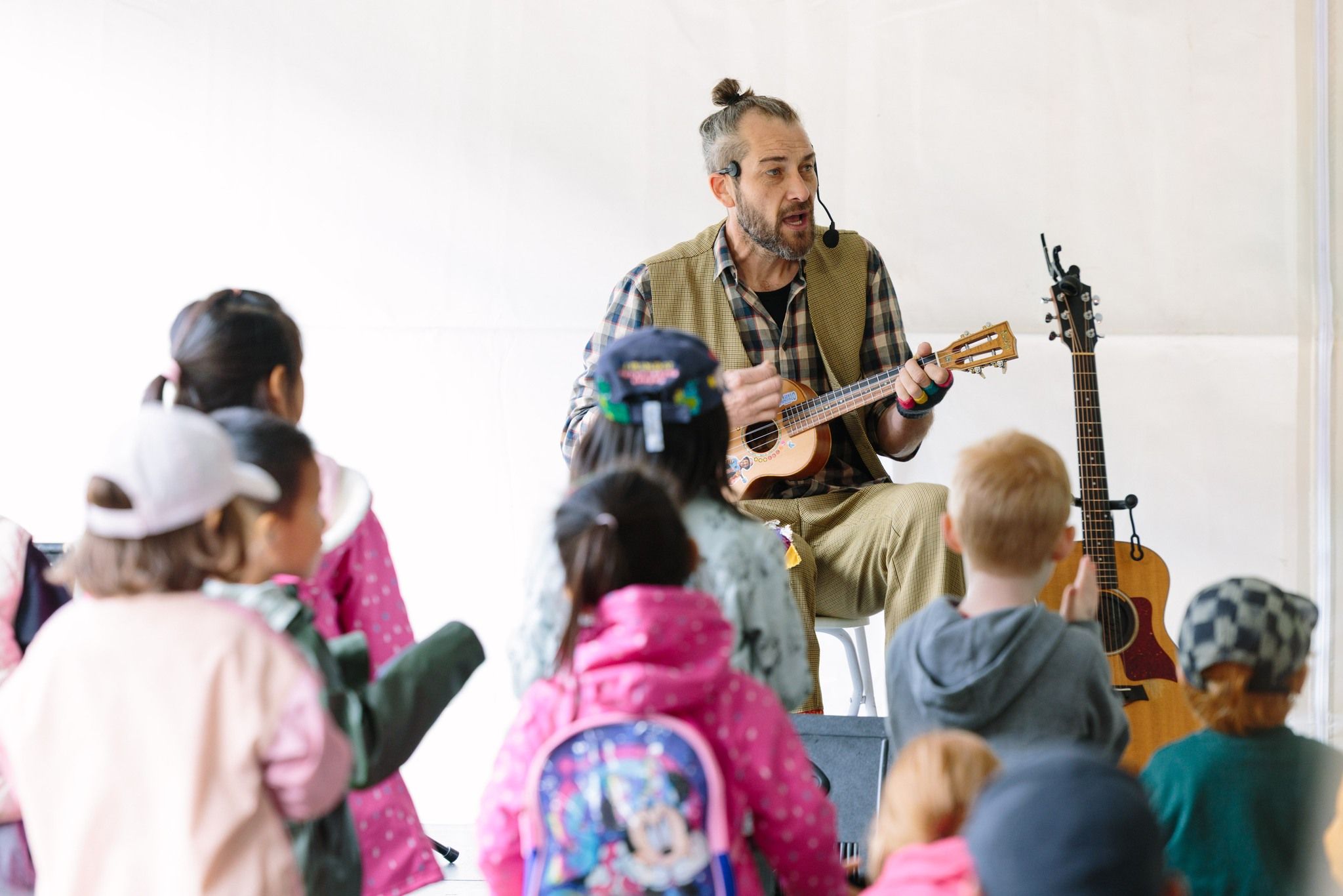 A performer plays music on a ukulele while entertaining a group of children sitting nearby. The kids watch and listen closely during this fun spring festival event. The Whistler Children’s Festival is known for family-friendly performances and activities.