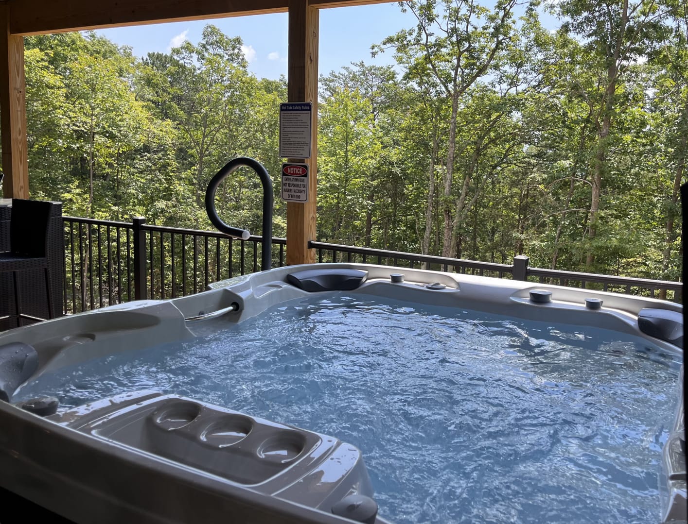 Covered outdoor hot tub filled with gently bubbling water on a private cabin deck, overlooking dense green forest views and surrounded by wood posts and railings for a peaceful, secluded mountain setting.