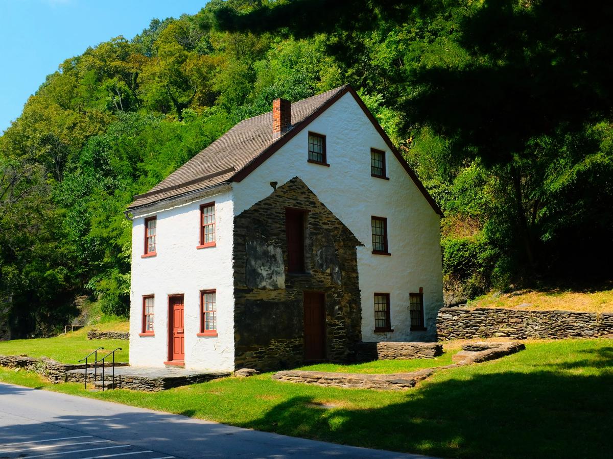 Old historical white house with red window frames and doors with greenery in the background in West Virginia