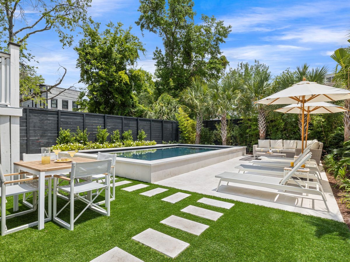 A sunny backyard with a private pool sits surrounded by palm trees and bright green landscaping. The lounge chairs, outdoor sofa, and dining table make the space perfect for relaxing or sharing meals outside. It feels calm, clean, and made for slow afternoons in the sun.